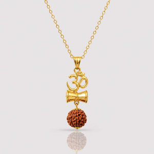 Gold Om symbol and Shiva hammer pendant necklace with a brown rudraksha bead dangling below, shown on a light gray background with a soft reflection.