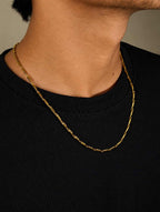 A close-up of a person's neck and upper chest wearing a gold chain necklace over a black ribbed crewneck shirt.