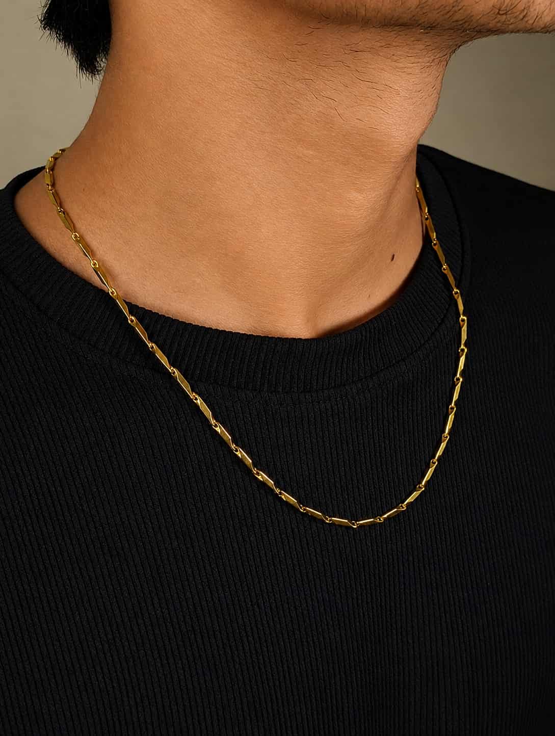 A close-up of a person's neck and upper chest wearing a gold chain necklace over a black ribbed crewneck shirt.