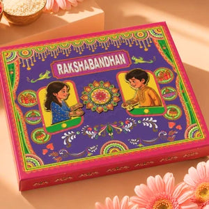 A decorative Rakshabandhan gift box with a purple front panel, pink edges, and colorful traditional illustrations, photographed on a warm beige surface with flowers and a small bowl in the background.