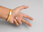 A gold textured bangle bracelet worn on a person's wrist, shown against a plain light gray background.