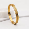 A gold band ring with a Greek key pattern engraved on the outer surface, displayed on a clean white surface.