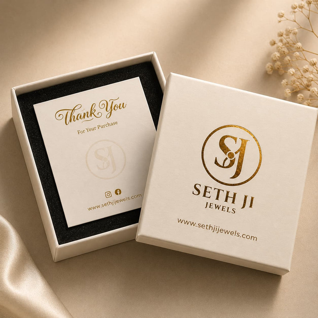 A premium jewelry gift box set from Seth Ji Jewels, featuring a white outer box with gold foil branding and a matching inner box with a thank you card, styled on a beige satin fabric background.