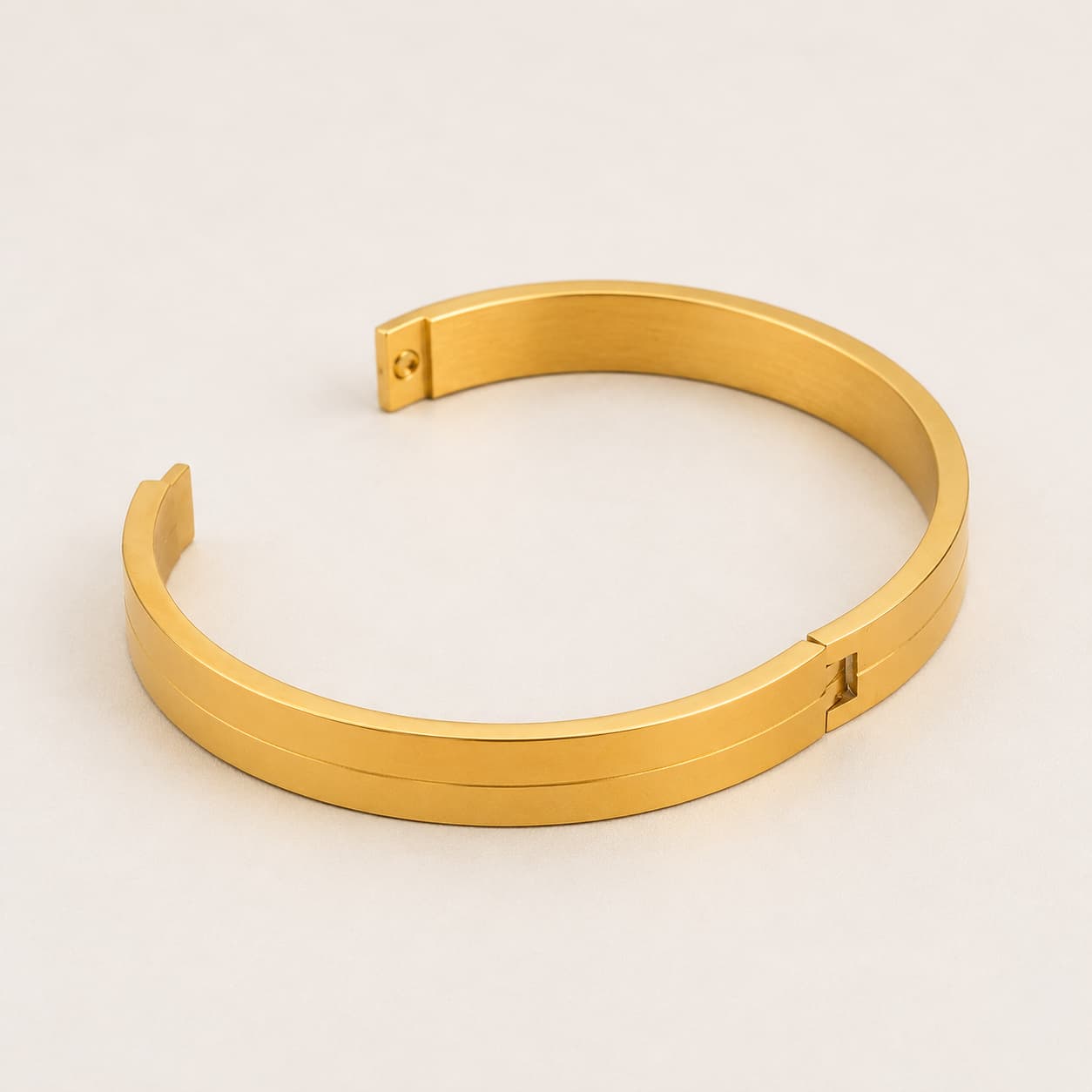 A polished gold-colored metal cuff bracelet with a minimalist design and a sliding clasp, displayed on a clean, light off-white background.