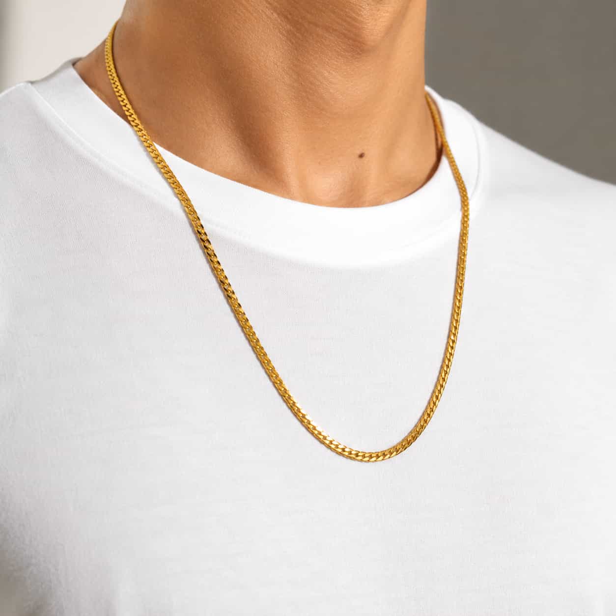 A close-up of a gold chain necklace worn around a person's neck over a white t-shirt.