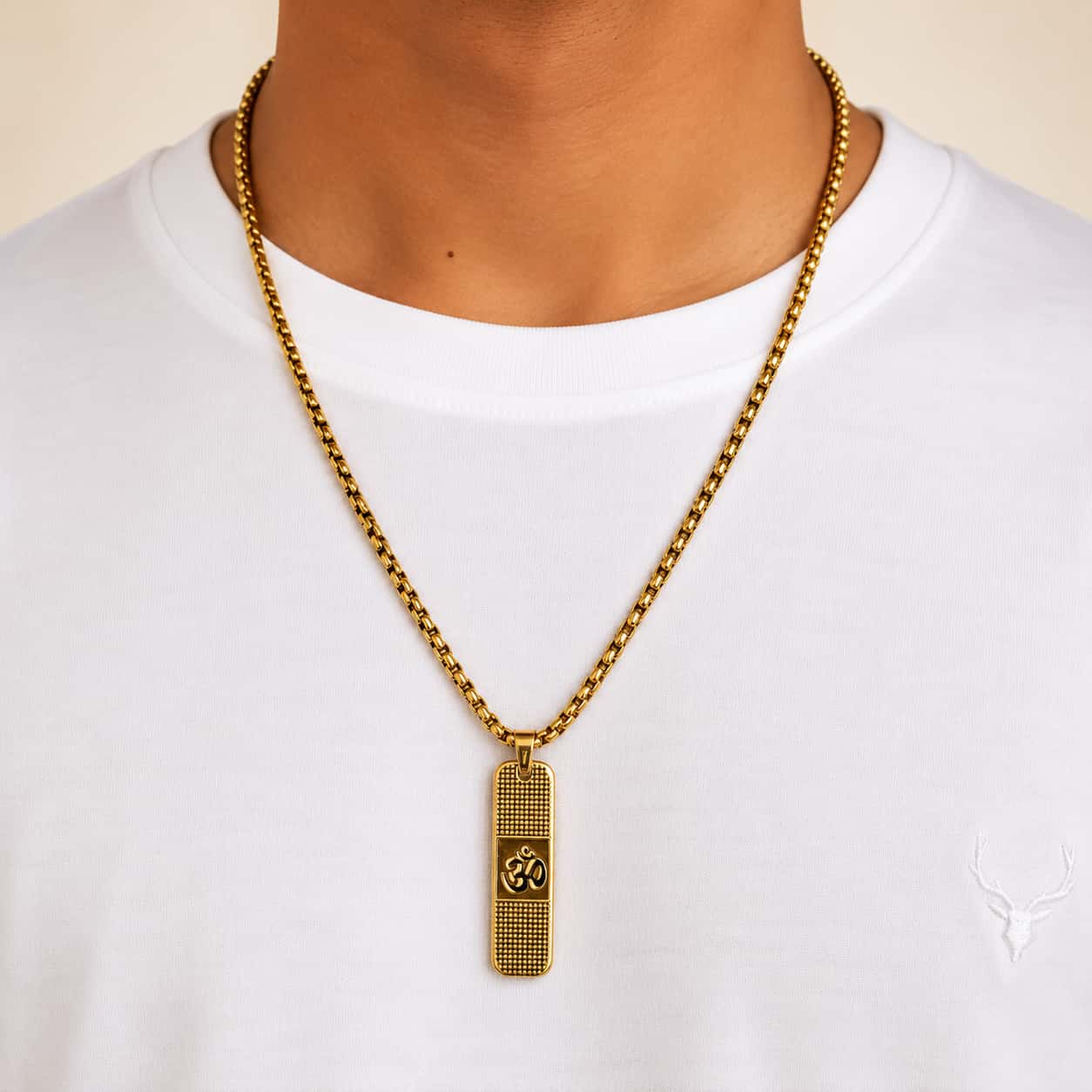 A gold chain necklace with a textured rectangular pendant featuring an Om symbol, worn by a model in a white t-shirt.