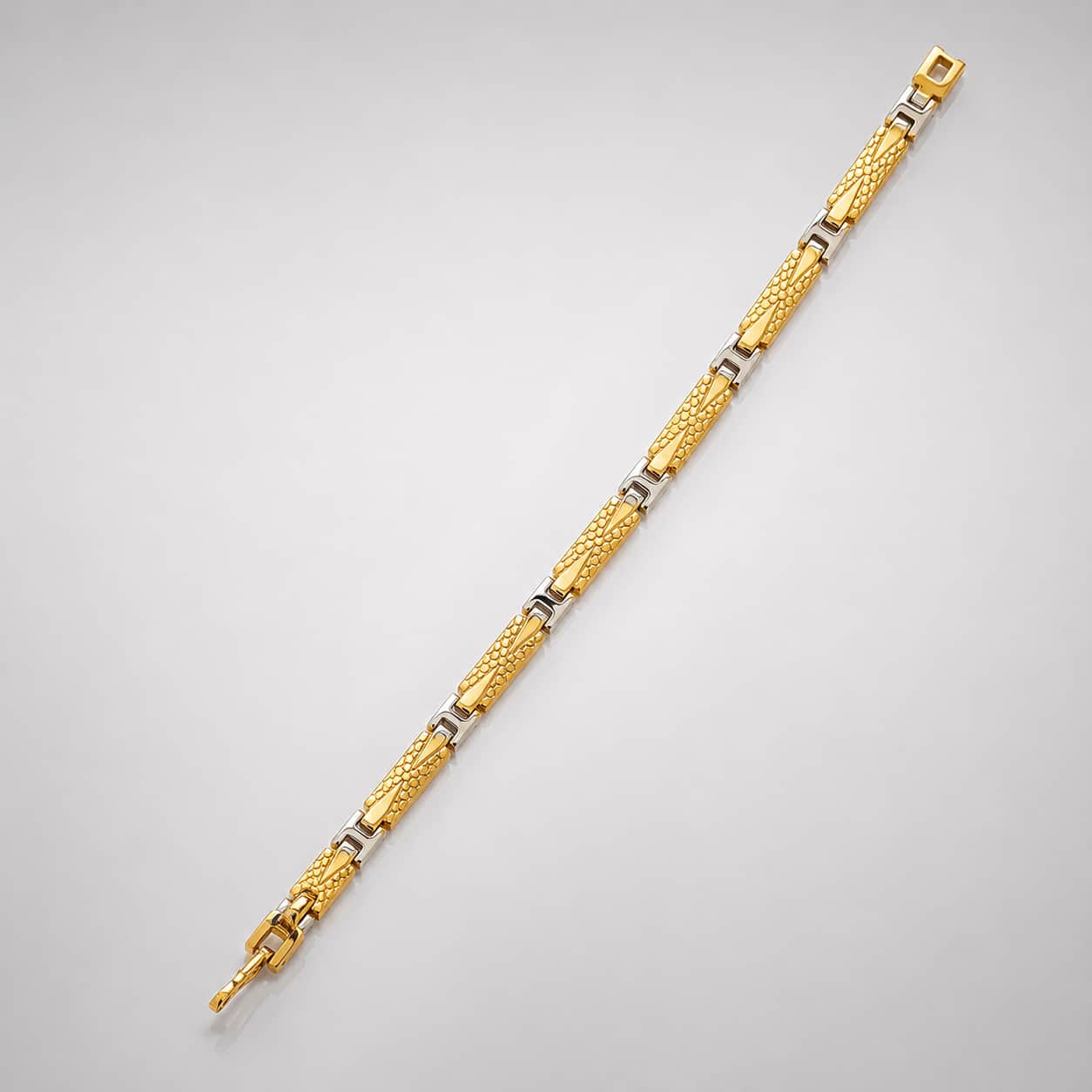 A gold-toned two-tone link bracelet with textured and polished segments, displayed diagonally on a light gray background.