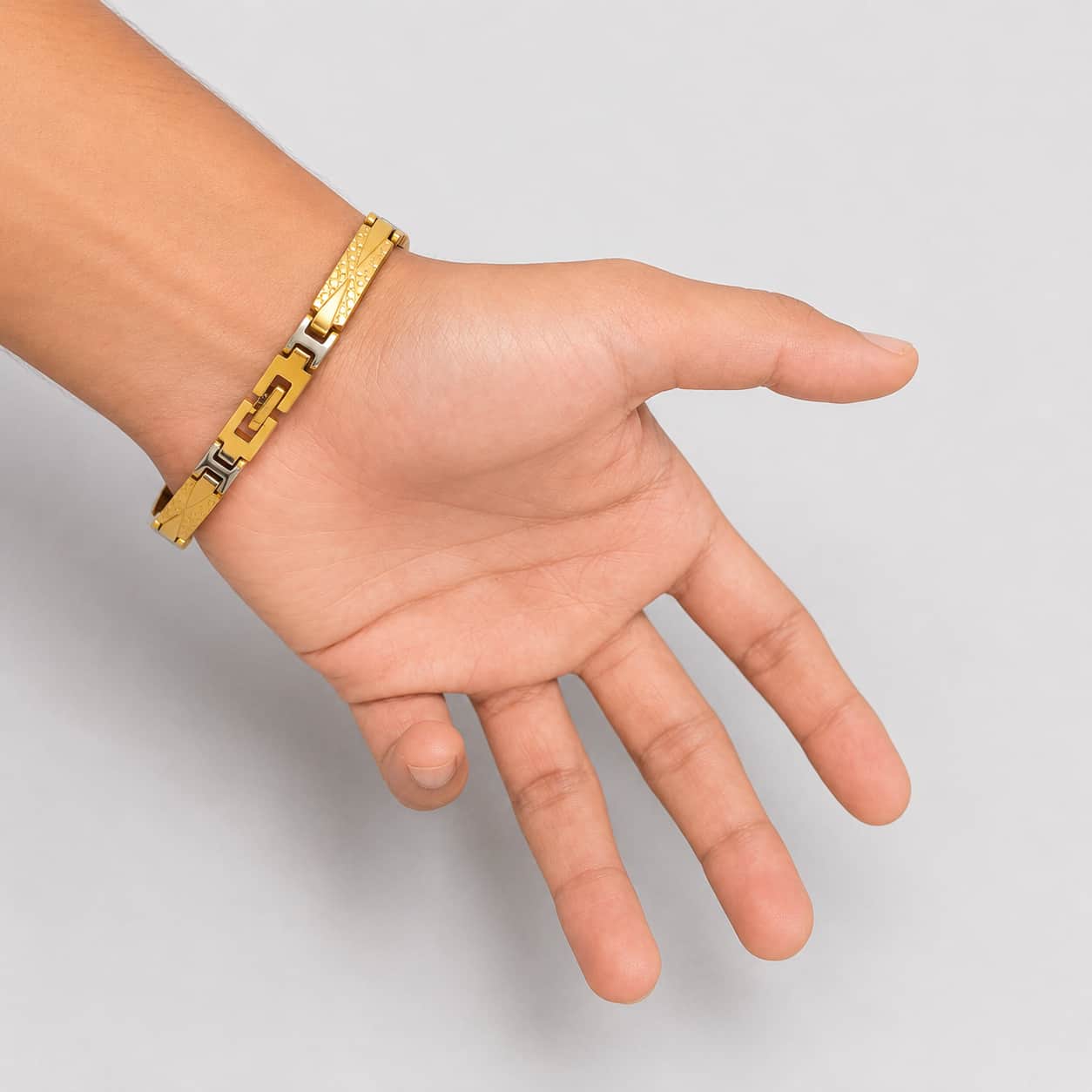 A gold-toned metal chain bracelet with textured and polished rectangular links, shown worn on a person's wrist with the hand palm facing forward against a light gray background.