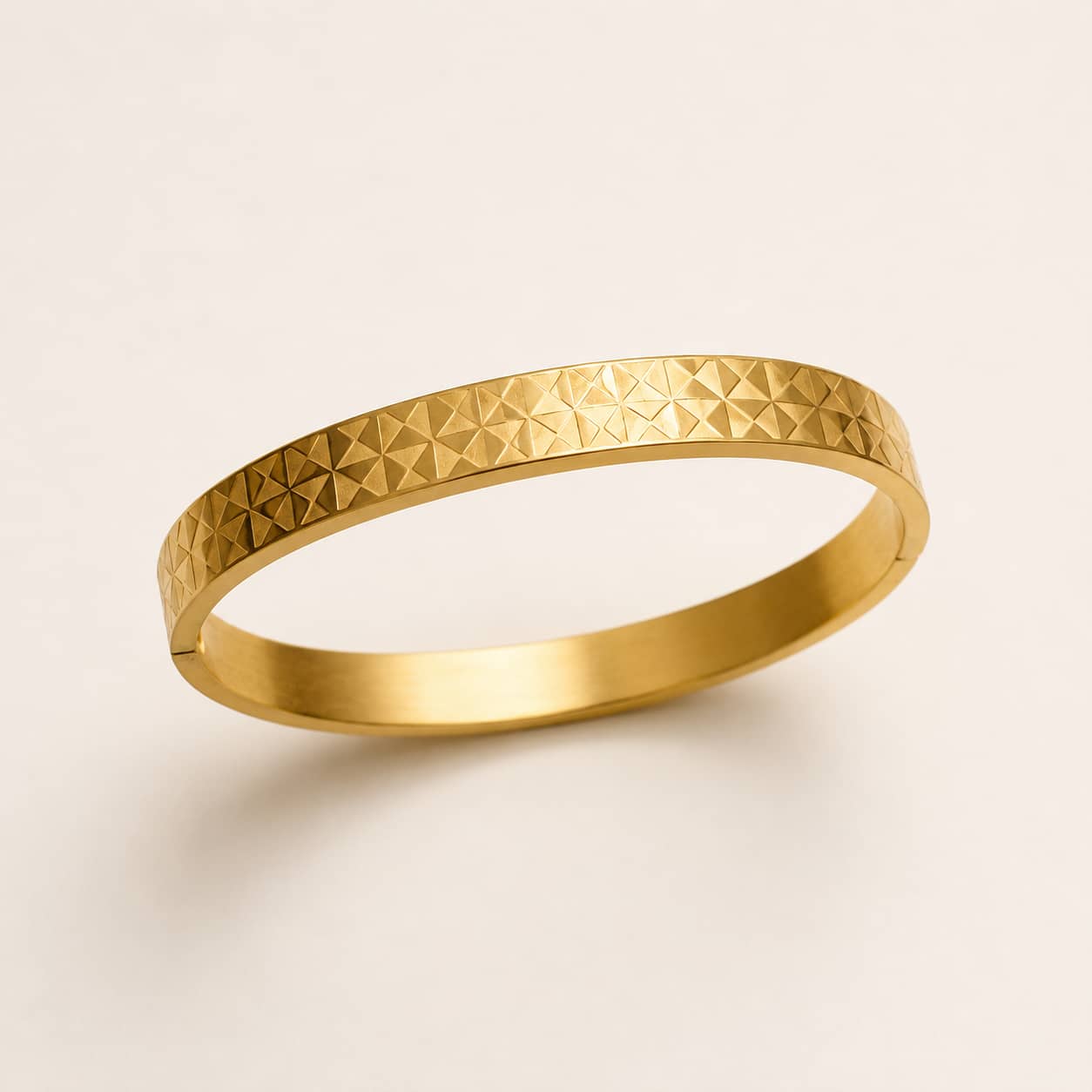 A gold bangle bracelet with a textured, geometric diamond-patterned exterior, shown on a clean off-white background.
