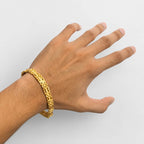A gold-toned geometric link bracelet worn on a person's wrist, shown against a plain light gray background.