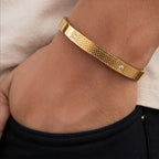 A gold-toned metal bangle bracelet with a textured honeycomb pattern and two small clear crystal accents, shown worn on a person's wrist.