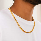 A close-up of a man wearing a chunky, textured gold chain necklace over a white t-shirt.