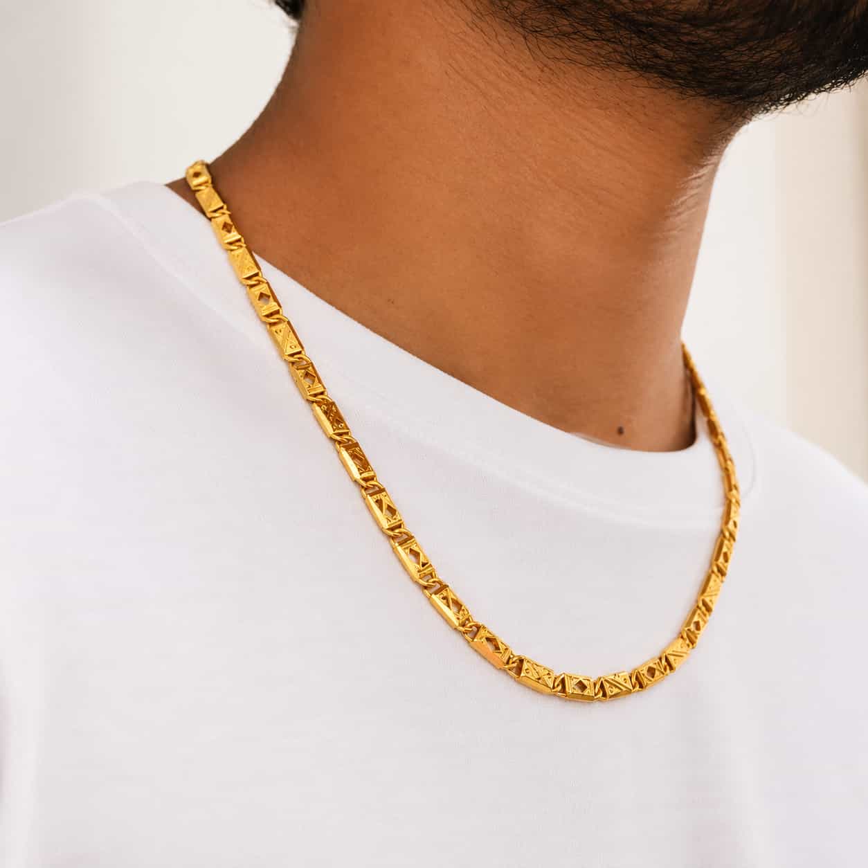 A close-up of a man wearing a chunky, textured gold chain necklace over a white t-shirt.