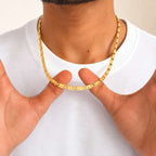 A close-up of a gold chain necklace worn around a person's neck, with both hands holding the chain at the front. The person is wearing a plain white t-shirt against a light neutral background.