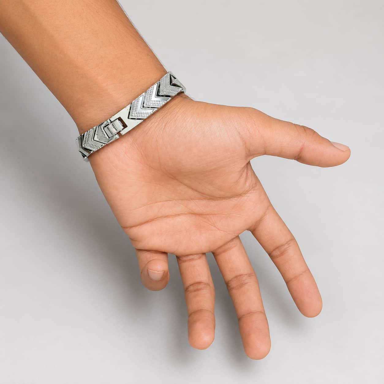 A silver-toned metal cuff bracelet with a geometric chevron pattern, shown worn on a person's wrist with their hand open against a plain light gray background.