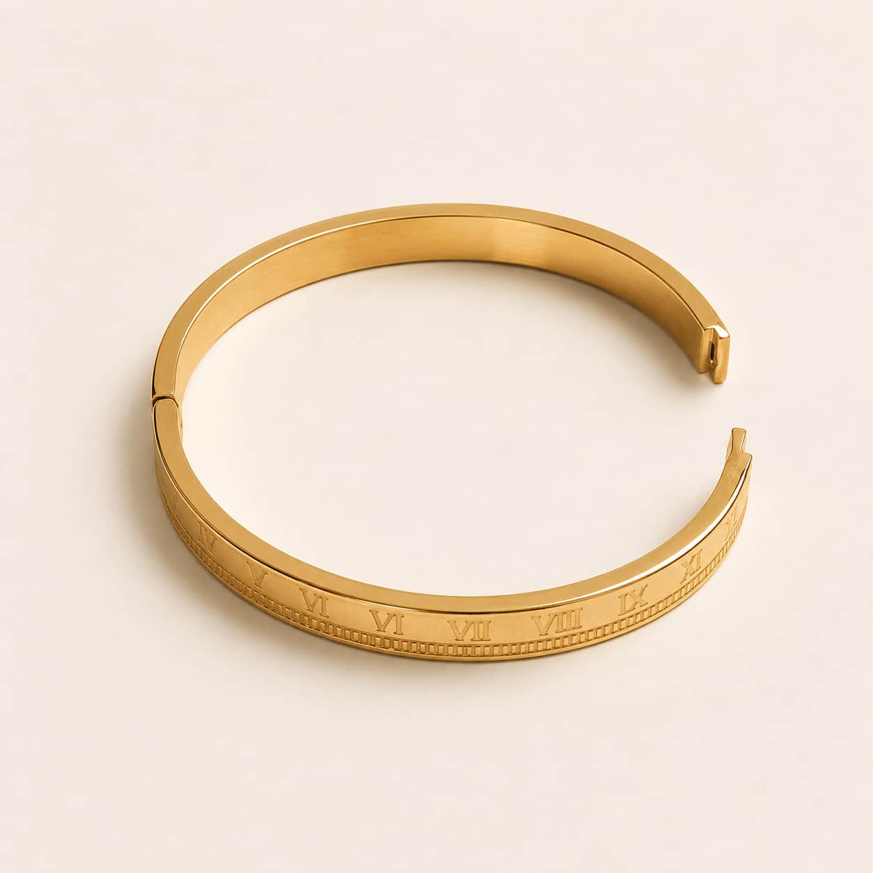 A polished gold-tone cuff bracelet with engraved Roman numerals on the outer band, displayed on a clean, light beige background.