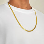 A close-up of a person wearing a slim, polished gold chain necklace over a white crewneck t-shirt.