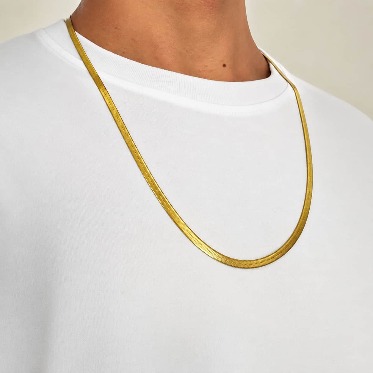 A close-up of a person wearing a slim, polished gold chain necklace over a white crewneck t-shirt.