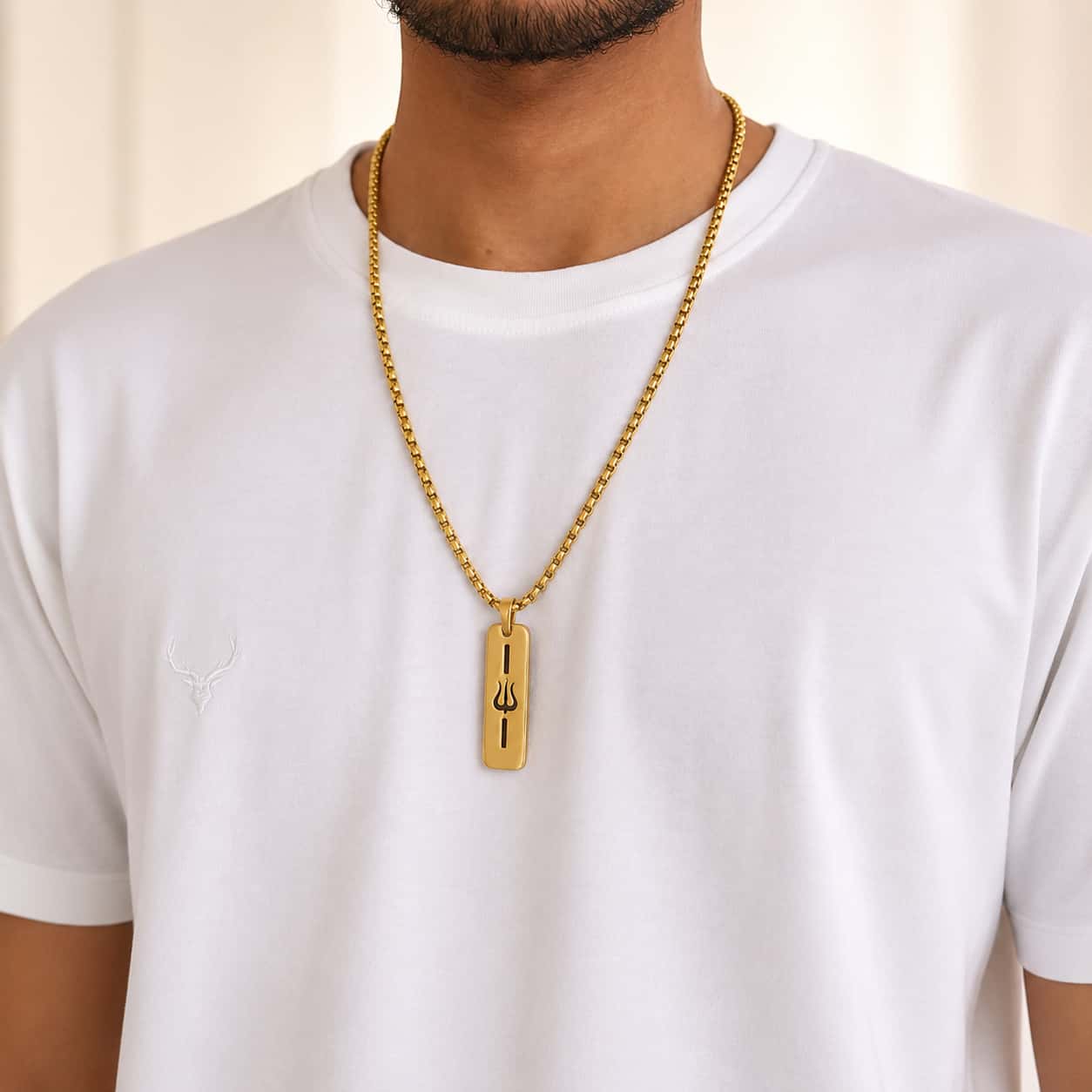 A gold chain necklace with a rectangular gold pendant featuring a black trident symbol, worn by a man in a white t-shirt.